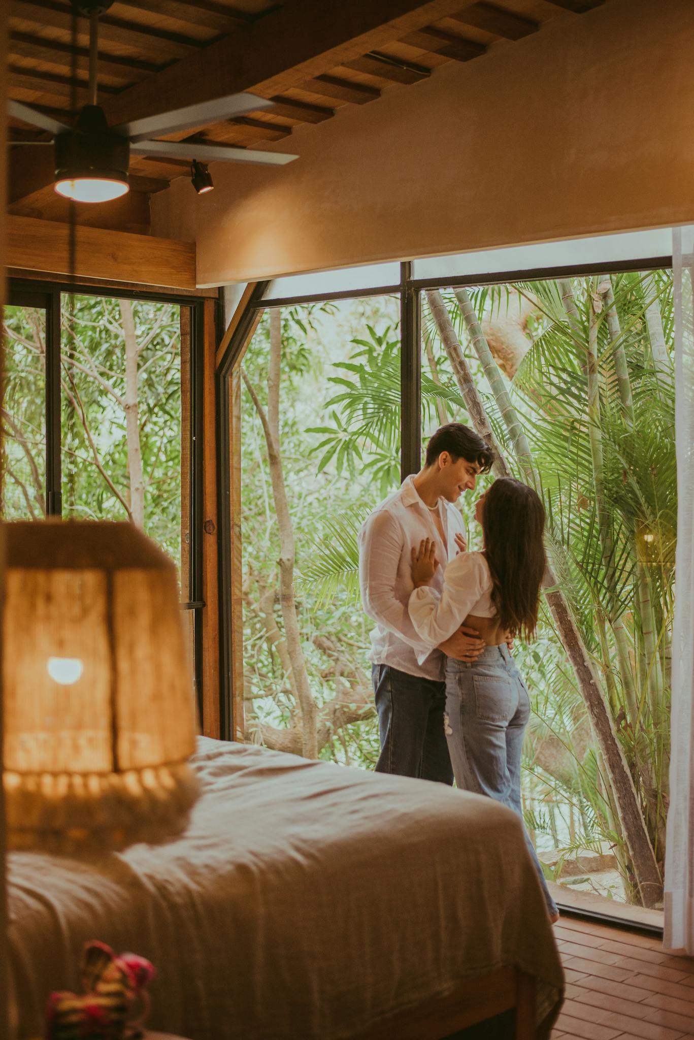 A couple shares a tender moment in a serene bedroom surrounded by nature, exuding warmth and romance.