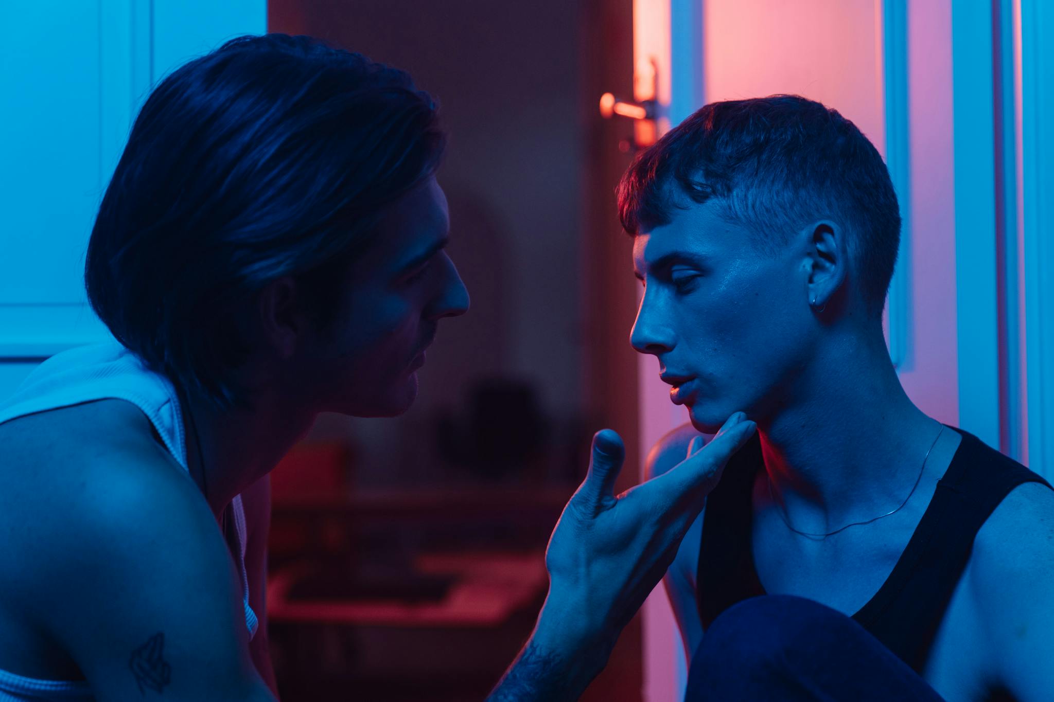 Intimate portrait of two men sharing a moment in atmospheric colored lighting.