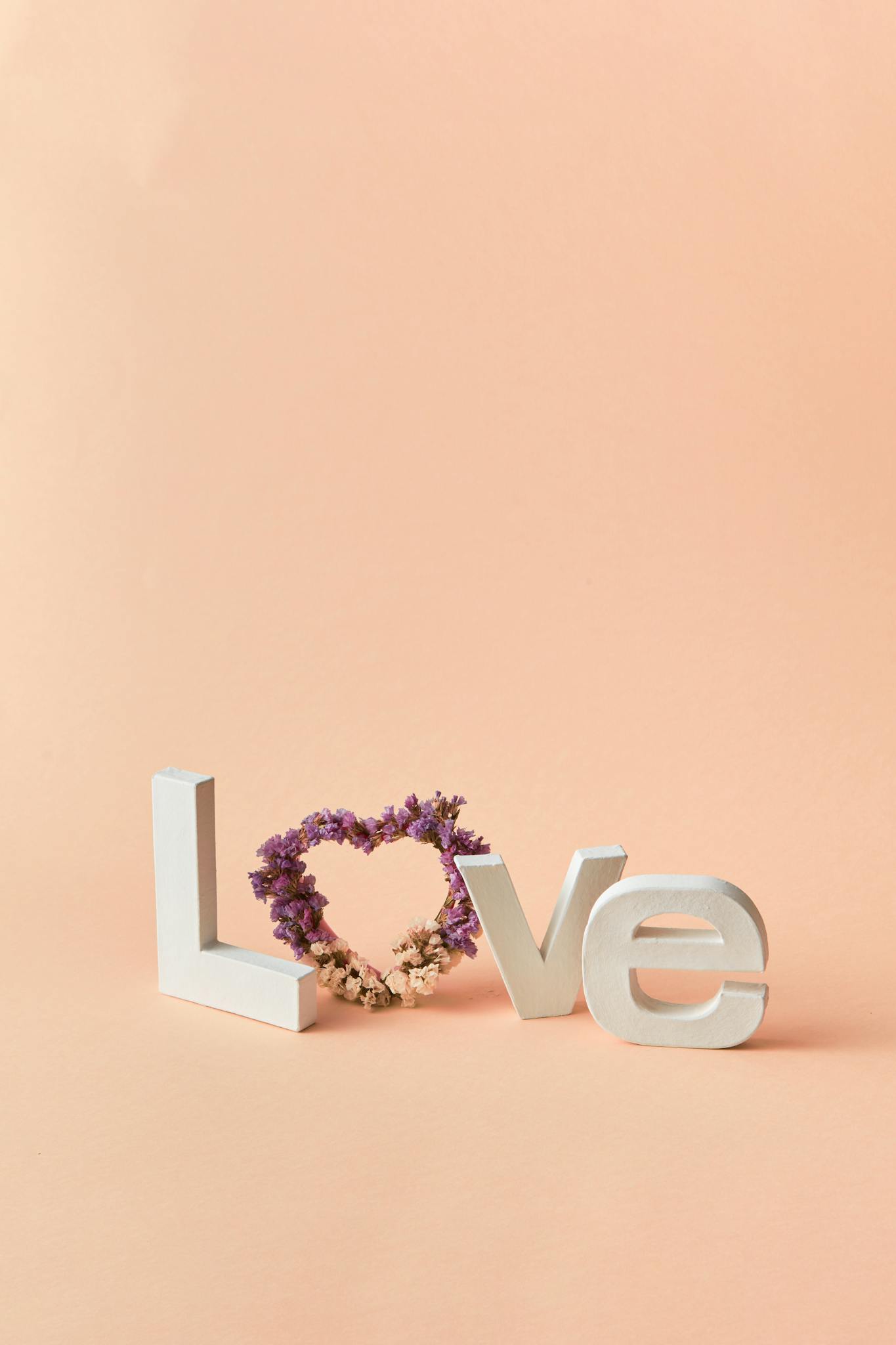 Minimalist design of love sign with heart-shaped floral arrangement on beige background. Perfect for romantic themes.